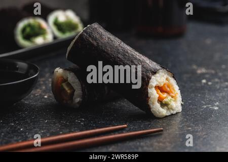 Eine Sushi-Rolle, die ordentlich auf einem schwarzen Tisch platziert ist, begleitet von einem Paar Essstäbchen, die zur Verwendung bereit sind. Das Sushi wirkt frisch und einladend, mit Fokus Stockfoto