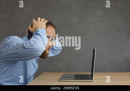 Verzweifelter Büroangestellter, der die Fehlermeldung auf dem Bildschirm seines Laptops ansieht Stockfoto