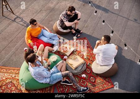Blick von oben auf fünf multirassische fröhliche Freunde, die gemeinsam Pizza und Cocktails auf der Dachparty genießen Stockfoto