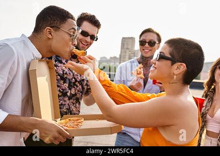 Multirassische fröhliche Menschen mit trendiger Sonnenbrille essen Pizza und trinken Cocktails auf der Party Stockfoto