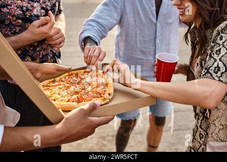 Zugeschnittene Ansicht von multikulturellen Freunden in lässigen, lebhaften Kleidern, die auf einer Party köstliche Pizza teilen Stockfoto