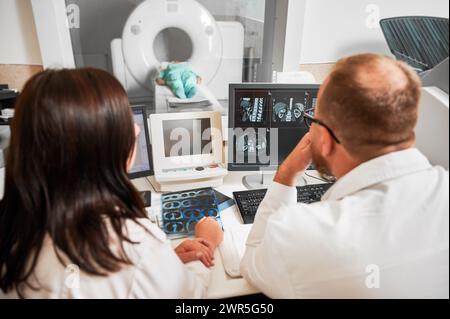 Medizinische Computertomographie oder MRT-Scanner. Rückansicht von zwei Ärzten, die am Computer sitzen und MRT machen. Zwei Spezialisten beraten, reden, denken, suchen. Konzept der modernen Diagnostik. Stockfoto