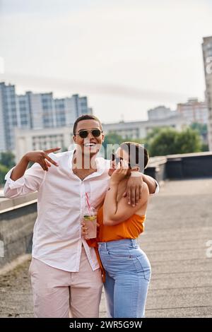 Fröhliche interrassische Mann und Frau in lässigen Kleidern, die auf einer Dachparty mit Cocktails chillen Stockfoto