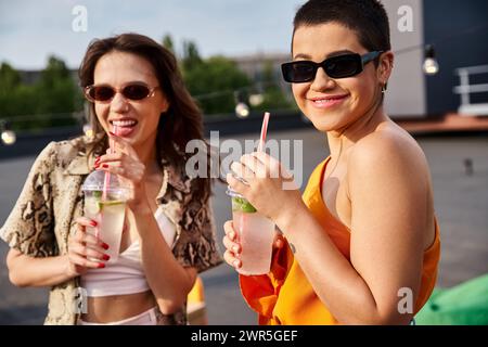 Fröhlich schöne Freundinnen, die Cocktails auf der Dachparty trinken und in die Kamera lächeln Stockfoto