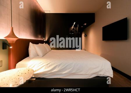 Ein High-End-Hotelzimmer mit einem geräumigen Bett und einem modernen Flachbildfernseher an der Wand schafft einen komfortablen und eleganten Raum für relaxa Stockfoto