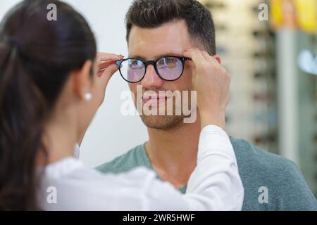 Gutaussehender Mann, der sich für eine Brille im Optikladen entscheidet Stockfoto