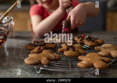 Das Mädchen putzt beim Backen Schokoladenfrost auf Weihnachtskekse Stockfoto