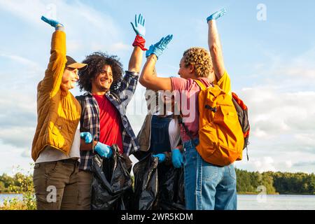 Fröhliche Gruppe von Freiwilligen, die nach einer Aufräumaktion am See triumphieren. Ecstatic Volunteers feiern einen erfolgreichen Lake Cleanup. Hochwertige Fotos Stockfoto