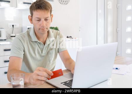 Junge Erwachsene Männer, die online mit Kreditkarte mit Laptop zu Hause einkaufen. Mann, der Kreditkarte hält und am Computer schreibt, um Warenbezahlung zu bestellen Stockfoto