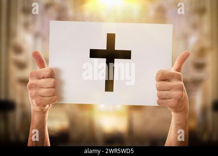 Hände eines religiösen Mannes mit einem OK-Schild, das ein weißes Poster mit gezeichnetem Kreuz mit kirchlichem Hintergrund hält Stockfoto