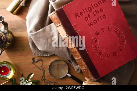 Altes und verschlechtertes Buch der Religionen der Welt mit eingravierten Buchstaben auf dem Cover und antiken Studien- und Abenteuergegenständen auf Holztisch. Stockfoto