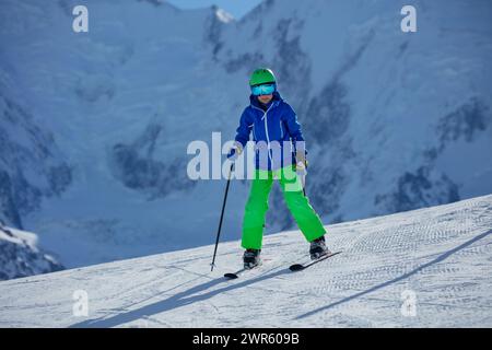 Die Skibrille ist ein Skifahrer mit Schutzausrüstung und hebt sich von der verschneiten Piste und der zerklüfteten Bergkulisse ab, während er hinuntergleitet Stockfoto