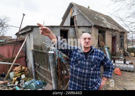 MYKOLAIV Reg, UKRAINE - 2. März 2024: Ein älterer Mann, ein ortsansässiger Bewohner, wird vor seinem beschädigten Haus gesehen und erzählt, was in seinem Dorf in der Region Mykolaiv passiert ist Stockfoto