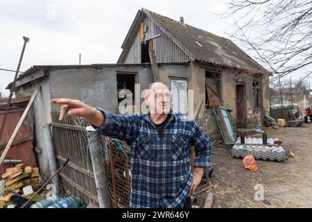 MYKOLAIV Reg, UKRAINE - 2. März 2024: Ein älterer Mann, ein ortsansässiger Bewohner, wird vor seinem beschädigten Haus gesehen und erzählt, was in seinem Dorf in der Region Mykolaiv passiert ist Stockfoto