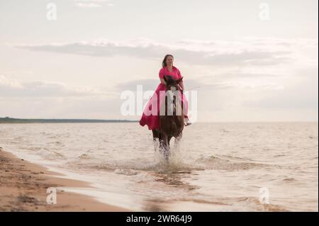 Eine Frau reitet anmutig auf einem Pferd im Wasser am Strand Stockfoto