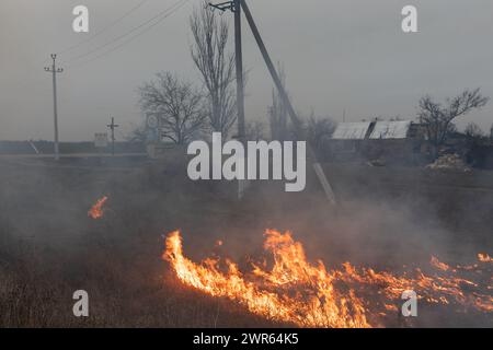 MYKOLAIV Reg, UKRAINE – 2. März 2024: Krieg in der Ukraine. Brennendes Gras am Rande eines Dorfes in der Region Mykolajew in der Ukraine. Stockfoto