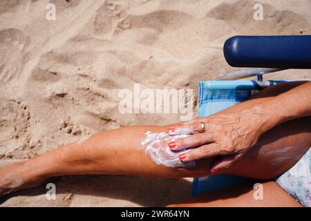Eine Frau trägt Sonnencreme auf ihre Beine, während sie sich in einem Liegestuhl sonnt. Prävention vor Hautkrebs. Körperpositivität Stockfoto