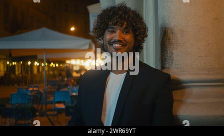 Hübscher indischer Latino-Arabian-Amerikaner glücklicher Geschäftsmann lächelnd in der Abendstraße vor der Jacke stehend und auf Kamera Zahnarzt blickt Stockfoto