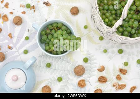 Ernte: Grüne Trauben im Korb und Nüsse auf einem Tisch mit Wasserkocher und Becher. Draufsicht. Stockfoto