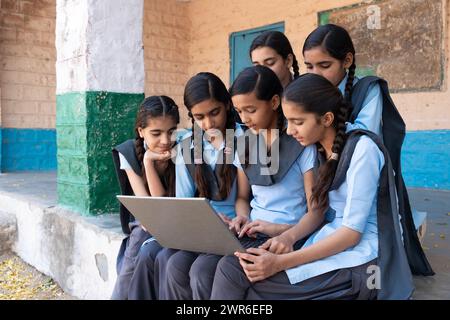 Gruppe ländlicher Schulmädchen in Uniform, die im Schulkorridor sitzen und am Laptop arbeiten - Konzept der digitalen Bildung Stockfoto