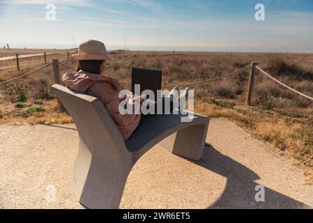 Frau mit Laptop, die vor dem Strand in Barcelona sitzt. Stockfoto