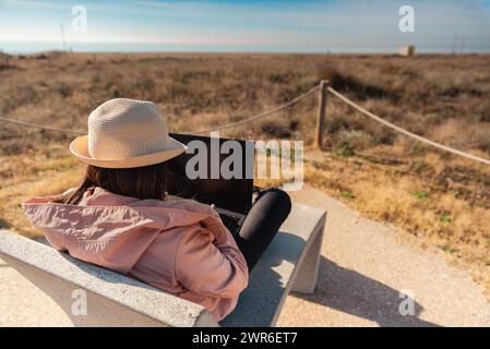 Frau mit Laptop, die vor dem Strand in Barcelona sitzt. Stockfoto