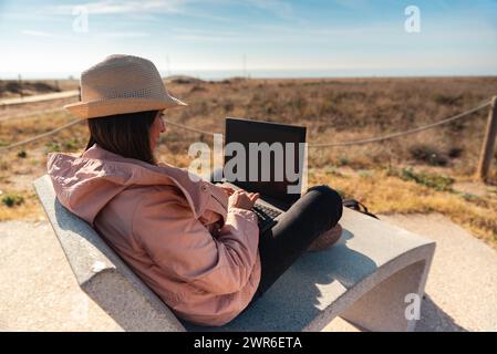 Frau mit Laptop, die vor dem Strand in Barcelona sitzt. Stockfoto