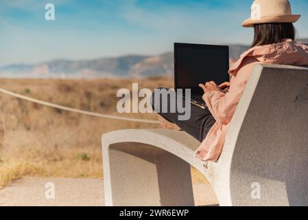 Frau mit Laptop, die vor dem Strand in Barcelona sitzt. Stockfoto