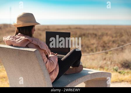 Frau mit Laptop, die vor dem Strand in Barcelona sitzt. Stockfoto