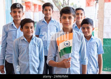 Gruppe glücklicher Dorfjungen in Schuluniform, die den Unabhängigkeitstag mit indischer Flagge in der Hand feiern - Konzept der Unabhängigkeit, Tag der republik, Patriotis Stockfoto