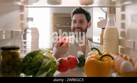 Blickwinkel von innen Kühlschrank POV Kaukasischer Mann Haushalter Hausbesitzer öffnen Kühlschrank Tür Küche voll mit Produkten Essen lächelnd finden Rot nehmen Stockfoto