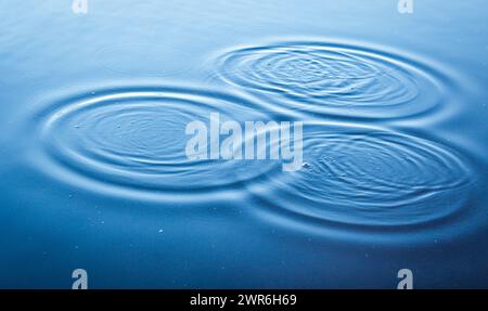 Runde Wassertröpfchen über Kreisen auf dem See. Wassertropfen, wirbeln und Spritzen. Telefon- und Laptop-Hintergrundbild. Nahaufnahme Wasserringe beeinflussen die Oberfläche. Stockfoto