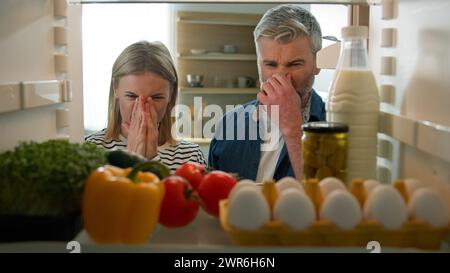 POV-Perspektive vom Inneren des Kühlschranks Erwachsenes Paar fühlte sich schlecht ekelhaft unangenehmer Geruch vom kaputten Kühlschrank verdorbenes verfaultes Essen in der Mitte Stockfoto