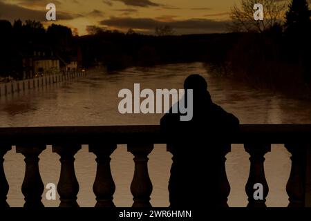 Die Silhouette einer Person mit Blick von der Bewdley Bridge auf den Fluss Severn darunter mit seinen platzten Ufern, die von den Flutschutzbarrieren der Stadt zurückgehalten werden. Stockfoto