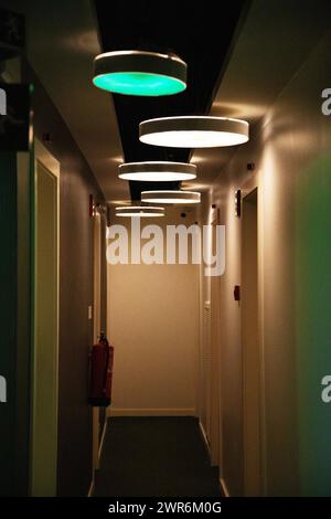 Ein schmaler Hotelkorridor, der von gedämpften Lichtern beleuchtet wird, schafft eine Atmosphäre der Intimität und Ruhe, die Gäste zum Entspannen einlädt Stockfoto
