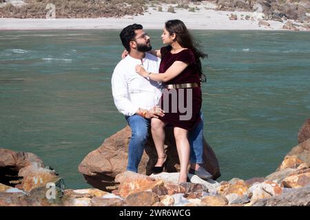 Romantik on the Rocks, Ein Paar, das von Angesicht zu Angesicht auf einem großen Felsen sitzt und von der malerischen Schönheit des Ganges in Rishikesh, Uttarakhand, umrahmt wird Stockfoto