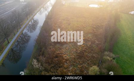 Der Sonnenaufgang taucht einen ruhigen Kanal und Pfad in ein warmes, trübes Licht und unterstreicht die Ruhe der natürlichen Landschaft. Nebelblick auf einen üppigen Canal Path bei Sonnenaufgang. Hochwertige Fotos Stockfoto