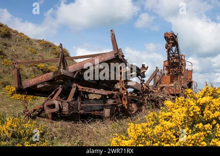 Rostiger alter, verrosteter Eisenbahnkran mit schweren Ketten, Rädern, Hebekran auf den Alderney Channel Islands mit gelbem Ginster und blauem Himmel Stockfoto