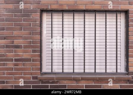 Eine Ziegelmauer mit einem Fenster mit den Jalousien und einem Sicherheitstor aus Metall Stockfoto