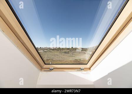 Dachfenster mit Holzstruktur und Metallgitter eines Dachzimmers mit Blick auf die Landschaft an einem Tag mit klarem blauem Himmel Stockfoto