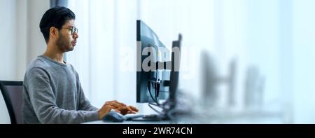Asiatischer Promt-Ingenieur entwickelt eine Codierungs-App mit Softwaredaten, die vor dem Computermonitor im Büro liegen Stockfoto