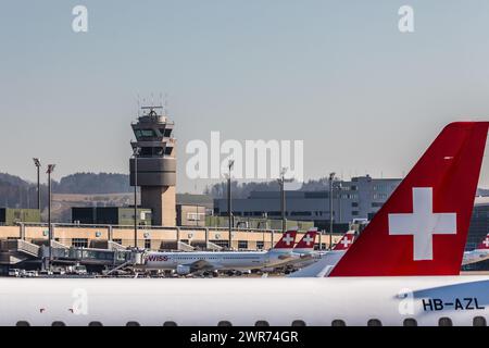 Zürich, Schweiz - 28. Februar 2022: Blick auf das Terminal A mit dem Kontrollturm des Flughafens Zürich. Eine Heckflosse eines Embraer Flugzeug der SC Stockfoto