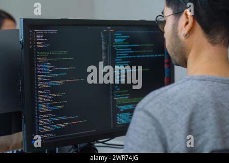 Asiatischer Promt-Ingenieur entwickelt eine Codierungs-App mit Softwaredaten, die vor dem Computermonitor im Büro liegen Stockfoto
