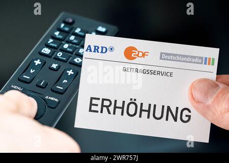 Deutschland - 11. März 2024: GEZ Gebührenerhöhung Symbolbild. Hand mit ARD, ZDF und Deutschlandradio Logo und der Aufschrift: Erhöhen vor Fernbedienung und Fernseher. PHOTOMONTAGE *** GEZ Gebühren Erhöhung Symbolbild. Hand mit ARD, ZDF und Deutschlandradio Logo und der Aufschrift: Erhöhung vor einer Fernbedienung und einem Fernseher. FOTOMONTAGE Stockfoto