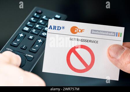 Deutschland - 11. März 2024: Bild des Symbols GEZ-Gebühren Abschaffung. Hand mit ARD, ZDF und Deutschlandradio Logo vor Fernbedienung und Fernseher. PHOTOMONTAGE *** GEZ Gebühren Abschaffung Symbolbild. Hand mit ARD, ZDF und Deutschlandradio Logo vor einer Fernbedienung und einem Fernseher. FOTOMONTAGE Stockfoto