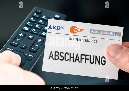 Deutschland - 11. März 2024: Bild des Symbols GEZ-Gebühren Abschaffung. Hand mit ARD, ZDF und Deutschlandradio Logo vor Fernbedienung und Fernseher. PHOTOMONTAGE *** GEZ Gebühren Abschaffung Symbolbild. Hand mit ARD, ZDF und Deutschlandradio Logo vor einer Fernbedienung und einem Fernseher. FOTOMONTAGE Stockfoto