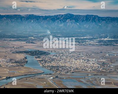 Aus der Vogelperspektive auf die Stadt Deltebre und das Ebro-Delta an einem Winternachmittag. Im Hintergrund das Hafenmassiv (Tarragona, Katalonien, Spanien) Stockfoto