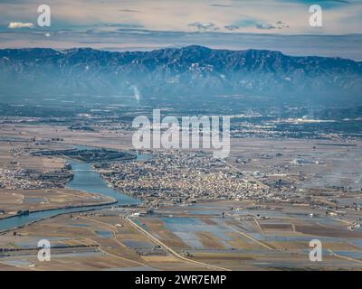 Aus der Vogelperspektive auf die Stadt Deltebre und das Ebro-Delta an einem Winternachmittag. Im Hintergrund das Hafenmassiv (Tarragona, Katalonien, Spanien) Stockfoto