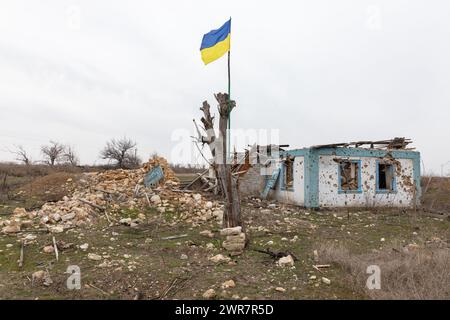 Region Mykolaiv, Ukraine. März 2024. Eine ukrainische Flagge ist an einem beschädigten Baum vor dem Hintergrund eines Wohngebäudes in einem Dorf in der Region Mykolajew angebracht, das von russischen Truppen vollständig zerstört wurde. Eine typische Szene eines ukrainischen Dorfes in der Region Mykolajew, wie in anderen Regionen der Ukraine nach der Besatzung und in der Nähe der Frontlinie. Regelmäßige Beschießung und Zerstörung von Häusern von Anwohnern. Quelle: SOPA Images Limited/Alamy Live News Stockfoto