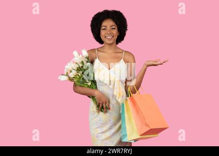 Strahlende afroamerikanische Frau, die freudig einen Strauß weißer Tulpen und bunter Einkaufstaschen hält Stockfoto